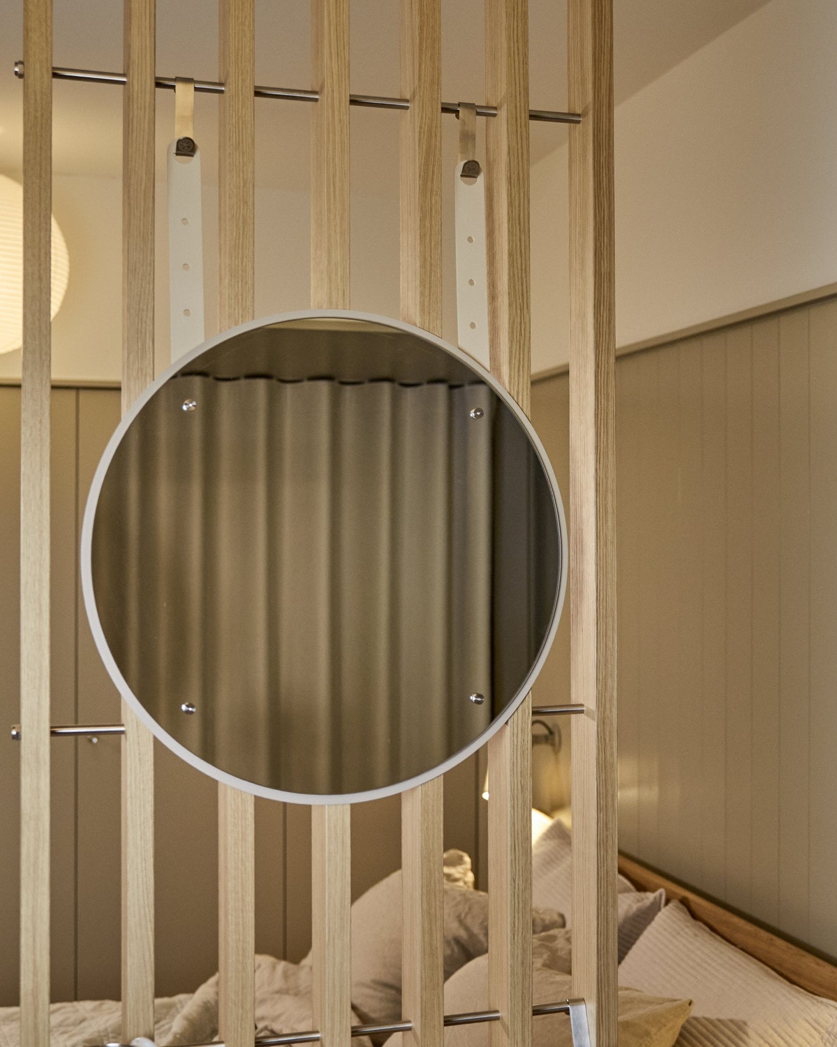 Ronde, in hoogte verstelbare Vala BM1 spiegel van WoodUpp, 54 cm diameter, gemonteerd op vertical akoestisch houten lattenpaneel met zachte neutrale verlichting.